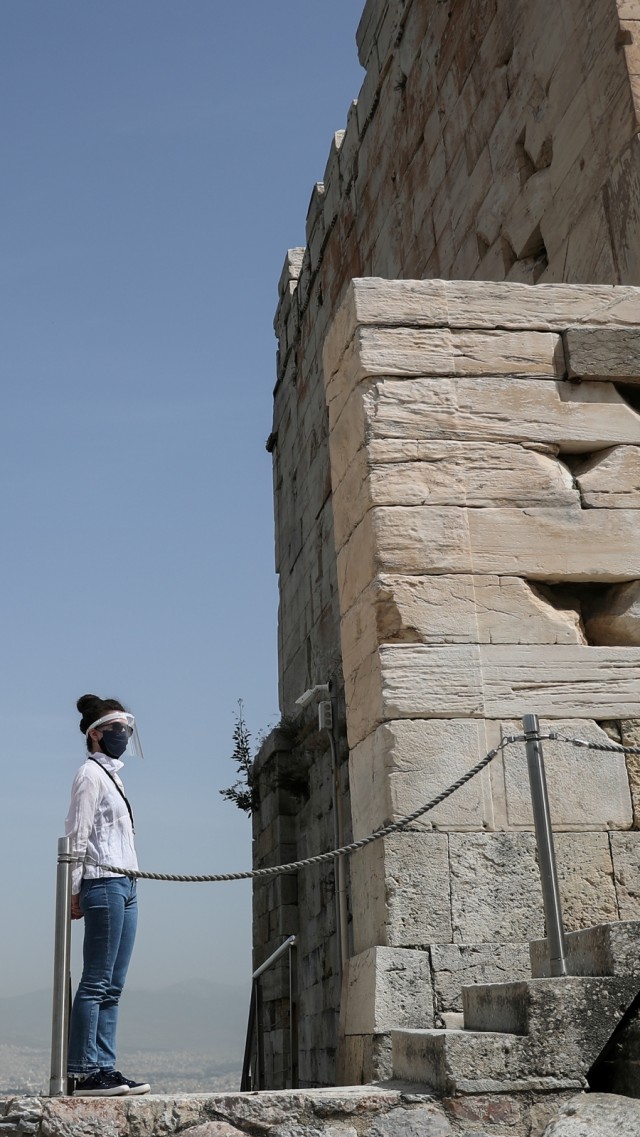 Seorang pegawai kementerian kebudayaan yang mengenakan pelindung wajah berdiri di Propylaea Acropolis, Athena, Yunani. Foto: REUTERS/Alkis Konstantinidis