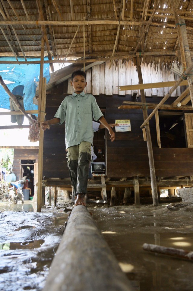 Seorang anak berjalan di atas kayu melintasi banjir di rumahnya. Foto: Abdul Hadi/acehkini 