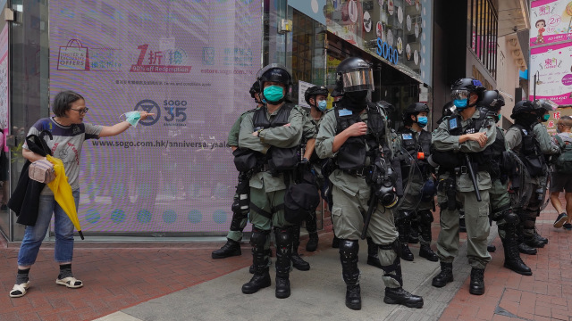 Polisi anti huru-hara berjaga ketika seorang wanita mencoba menyeberang jalan di distrik Tengah Hong Kong, Rabu, (27/5). Foto: AP Photo/Vincent Yu
