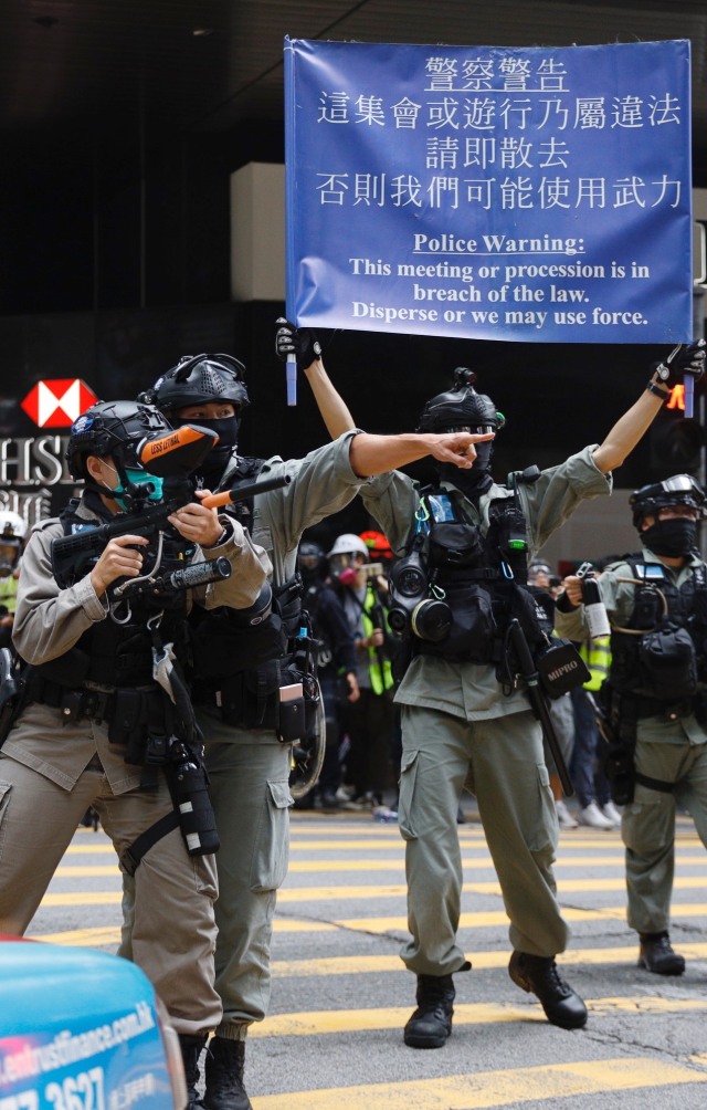Seorang perwira polisi anti huru hara menembakkan senjatanya selama demonstrasi di Kompleks Pemerintah Pusat di Hong Kong, Rabu, (27/5). Foto: AP Photo/Kin Cheung