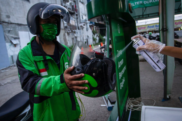Petugas menyemprotkan cairan disinfektan ke helm penumpang ojek online di kawasan Jl. Kendal, Jakarta, Senin (8/6). Foto: Antara/Dhemas Reviyanto
