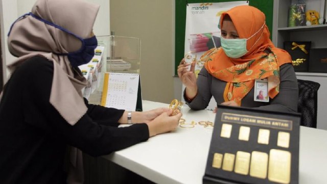Foto : Pegawai Mandiri Syariah melayani nasabah yang tengah bertransaksi Gadai Emas di Kantor Cabang Rasuna Said Kuningan, Jakarta dengan menggunakan protokal kesehatan covid-19. (sumber : detik.com)
