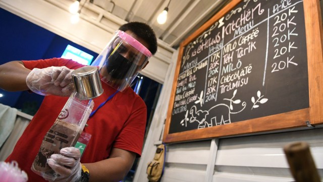 Seorang pedagang dengan mengenakan masker, pelindung wajah dan sarung tangan plastik meracik minuman saat pembukaan kembali pusat kuliner Thamrin 10. Foto:  ANTARA FOTO/M Risyal Hidayat