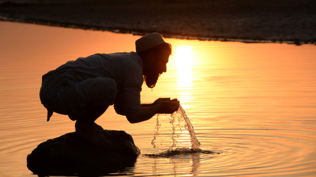 Seorang pria melakukan wudhu sebelum shalat di sebuah sungai. Foto: AFP