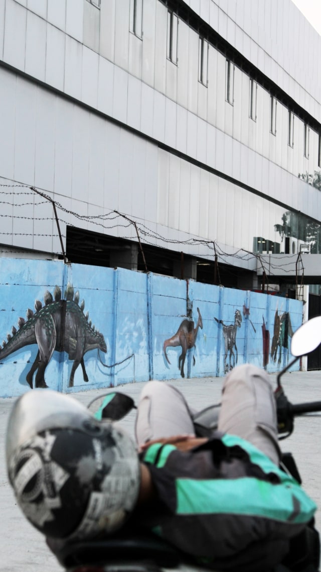 Pengendara ojek online tidur di atas motor di dekat mural di bantaran Kali Opak, Penjaringan, Jakarta Utara, Sabtu (27/6). Foto: Faisal Rahman/kumparan
