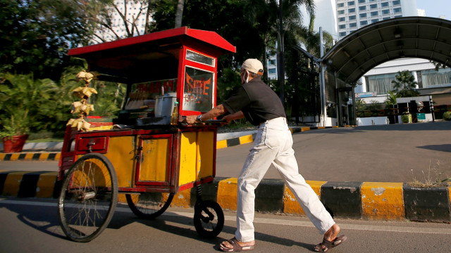Seorang pedagang kaki lima mendorong gerobaknya melintasi jalan di Jakarta. Foto: Willy Kurniawan/REUTERS