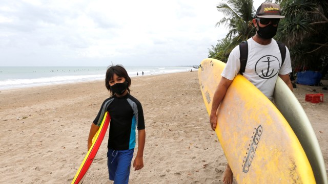 Turis asing membawa papan selancar mereka di pantai Kuta, Bali, Kamis (9/7). Foto: Firdia Lisnawati/AP Photo