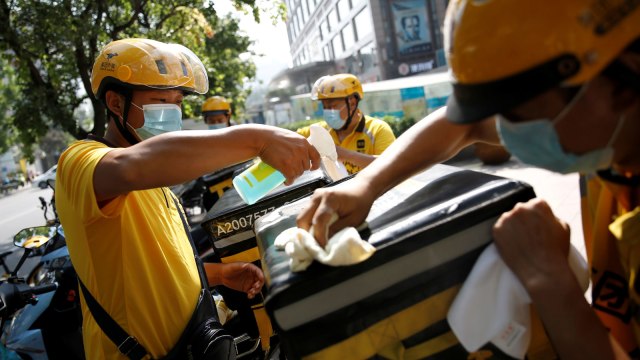 Kurir makanan Meituan Dianping membersihkan dan mendesinfeksi tempat paket yang akan dikirimkan Foto: TINGSHU WANG/Reuters