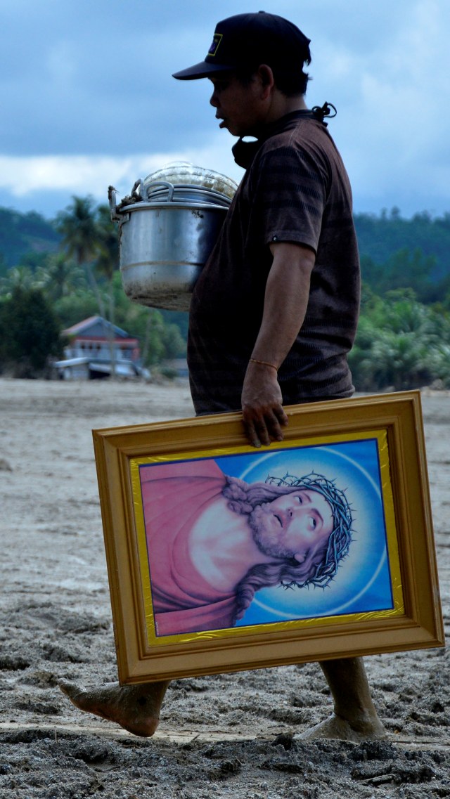 Warga membawa lukisan melewati material lumpur di Desa Radda, Kabupaten Luwu Utara, Sulawesi Selatan, Sabtu (18/7). Foto: Abriawan Abhe/ANTARA FOTO