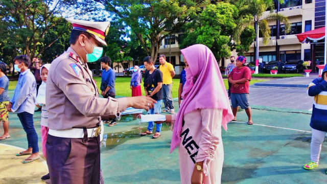 Salah seorang anggota polisi membagikan masker dan hand sanitizer kepada warga. Selasa, (21/7). Foto: Dok banthayoid (Herman Abdullah)