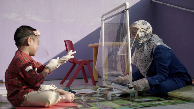 Seorang guru mengenakan pelindung wajah dan masker berbicara dengan siswanya di rumah mereka, di Semarang, Jawa Tengah. Foto: Stringer/REUTERS