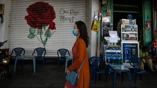 Seorang wanita berjalan melewati toko tertutup di sepanjang jalan di Kota Ho Chi Minh, Vietnam. Foto: Manan VATSYAYANA/AFP
