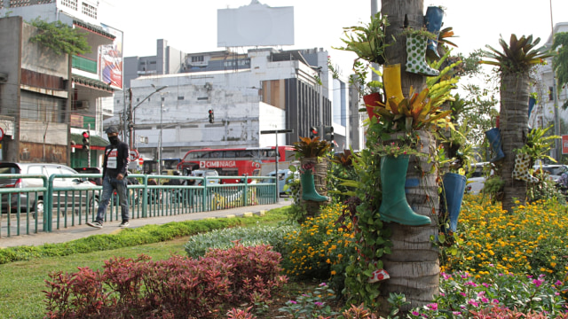 Pejalan kaki yang mengenakan masker melintasi taman yang dihias menggunakan sepatu boots warna-warni di Kawasan Kota Tua, Jakarta Pusat, Jumat (7/8). Foto: Faisal Rahman/kumparan