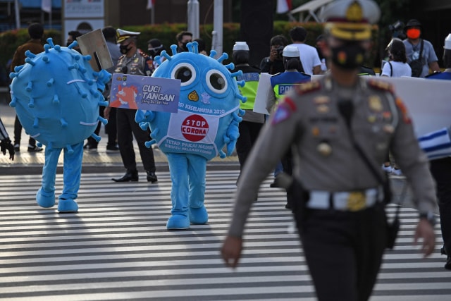 Petugas yang mengenakan kostum berbentuk virus corona membawa poster saat sosialisasi penggunaan masker di kawasan Sarinah, Jakarta. Foto: Wahyu Putro A/Antara Foto