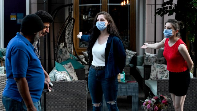 Karyawan yang mengenakan masker pelindung mengantar orang yang lewat untuk mengunjungi restoran mereka di sepanjang jalan pejalan kaki di pusat Tbilisi, Georgia. Foto: Vano SHLAMOV / AFP