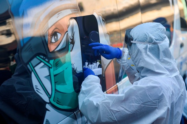 Seorang tenaga kesehatan yang mengenakan alat pelindung diri lengkap memberikan sample tes usap (swab test) milik warga ke dalam mobil tes polymerase chain reaction (PCR). Foto: M Risyal Hidayat/Antara Foto