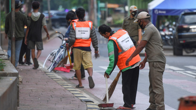 Warga yang melanggar aturan pemberlakuan Pembatasan Sosial Berskala Besar (PSBB) dihukum menyapu usai terjaring Operasi Tertib Masker di kawasan Kota Tua, Jakarta, Minggu (27/9). Foto: Hafidz Mubarak A/ANTARA FOTO