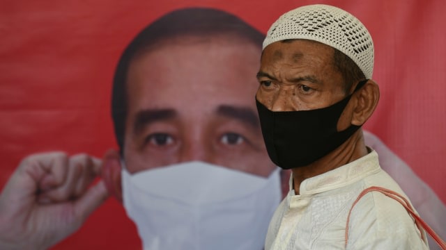 Seorang calon penumpang yang mengenakan masker scuba melintas di depan poster Presiden Joko Widodo saat akan memasuki Stasiun Tanah Abang, Jakarta. (Foto: M Risyal Hidayat/ANTARA FOTO)