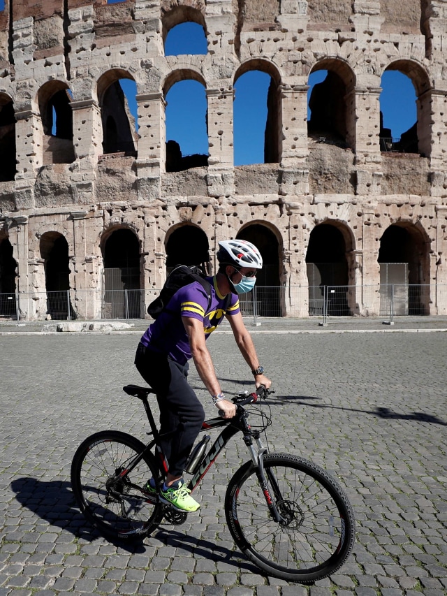 Warga mengenakan masker saat bersepeda melewati Colosseum ketika otoritas lokal di ibu kota Italia Roma memerintahkan agar mengenakan masker setiap saat di luar ruangan. Foto: Guglielmo Mangiapane/Reuters