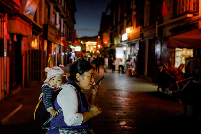 Seorang wanita yang menggendong bayi menggunakan ponsel di sebuah pasar di kota tua Lhasa, Tibet, China, Rabu (14/10/2020). Foto: THOMAS PETER/REUTERS
