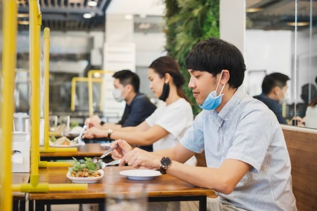 Orang yang sedang makan di restoran dengan mematuhi protokol