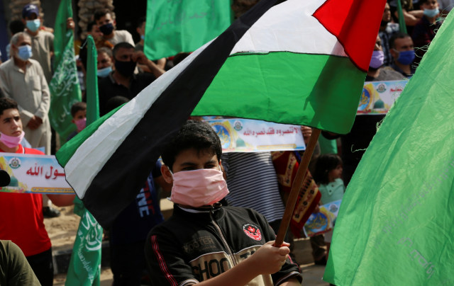 Pendukung Hamas memakai masker wajah sambil mengibarkan bendera nasional saat protes terhadap Presiden Prancis Emmanuel Macron, di jalan utama kamp pengungsi Jebaliya, Jalur Gaza, Jumat, (30/10). Foto: Adel Hana/AP Photo