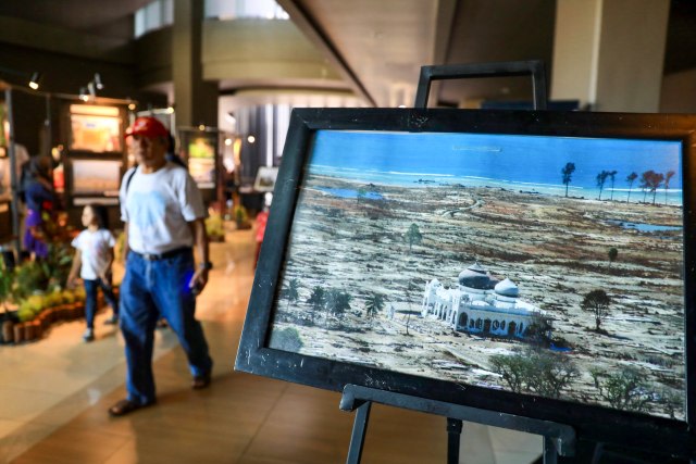 Warga melintas di antara foto-foto yang dipajang pada pameran foto kebencanaan 'Tanah Retak' di Museum Tsunami Aceh, Jumat (13/12/2019). Foto: Suparta/acehkini