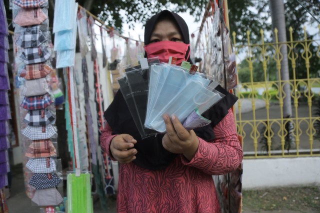 Seorang pedagang memperlihatkan masker yang dijualnya di pinggir jalan Teuku Umar, Banda Aceh, Senin (14/12) sore. Foto: Abdul Hadi/acehkini
