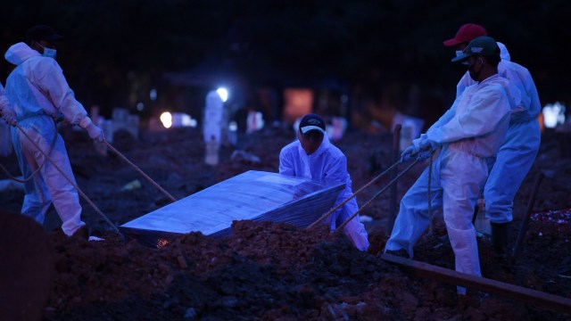 Petugas yang mengenakan APD memakamkan jenazah dengan protokol COVID-19 di TPU Tegal Alur, Jakarta, Selasa (29/12).  Foto: Wahyu Putro A/ANTARA FOTO