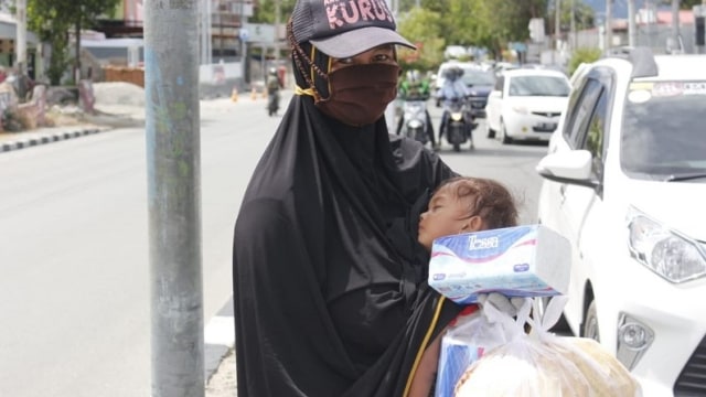 Yuliana (35) sambil menggendong anaknya jualan kripik dan tisu di seputaran traffic light (lampu lalulintas) Jalan Juanda, Kota Palu, Sulawesi Tengah. Foto: Rian/PaluPoso