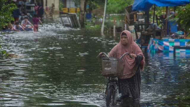 Warga menuntun sepedanya melintasi banjir yang merendam Jalan Prona di Banjarmasin, Kalimantan Selatan, Kamis (14/1). Foto: Bayu Pratama S/ANTARA FOTO