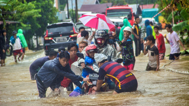 Sejumlah relawan membantu pengendara sepeda motor agar tidak terbawa arus saat melintas di Jalan Ahmad Yani, Kabupaten Banjar, Kalimantan Selatan, Jumat (15/1). Foto:  Bayu Pratama S/ANTARA FOTO