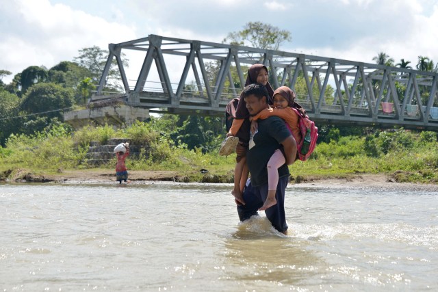 Warga menggendong anaknya saat menyeberangi sungai sepulang sekolah di wilayah pedalaman desa Panca, Kecamatan Lembah Seulawah, Kabupaten Aceh Besar, Aceh, Jumat, (22/1). Foto: Ampelsa/Antara Foto