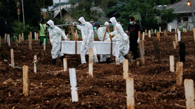 Petugas yang mengenakan APD membawa peti berisi jenazah dengan protokol COVID-19 di TPU Srengseng Sawah, Jakarta, Senin (25/1). Foto: Willy Kurniawan/REUTERS