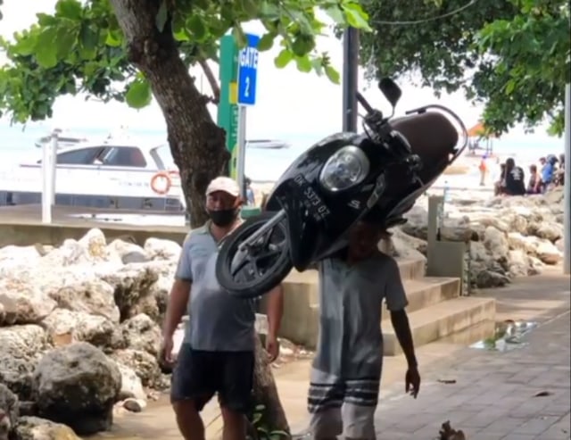 Seorang pria terlihat sedang mengangkat Honda Scoopy. Foto: Instagram @jukir_saras