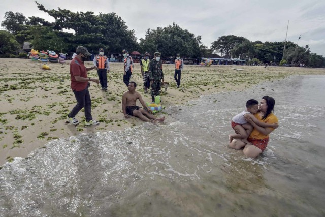 Petugas menegur warga yang beraktivitas tanpa menggunakan masker di Pantai Sanur, Denpasar, Bali, Minggu (31/1/2021). Foto: Nyoman Hendra Wibowo/ANTARA FOTO
