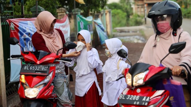 Seorang ibu memakaikan masker untuk anaknya saat masuk sekolah. Foto: Suparta/acehkini