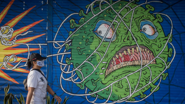 Warga melintas di depan mural bertema COVID-19 di Kemplayan, Solo, Jawa Tengah, Minggu (21/2/2021). Foto: Mohammad Ayudha/ANTARA FOTO