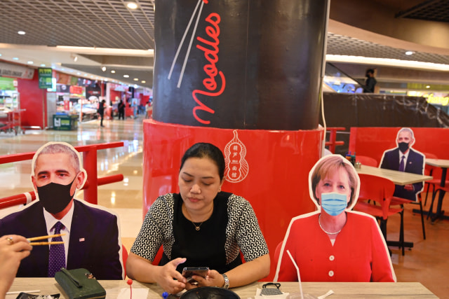 Pengunjung makan di samping gambar para pemimpin dunia yang ditempatkan untuk memastikan physical distancing di sebuah restoran di Jakarta. Foto: Adek Berry/AFP