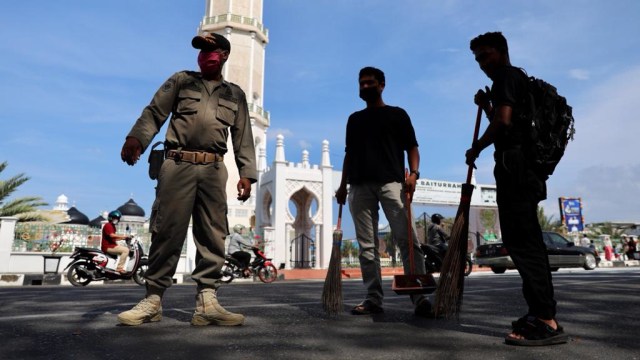 Warga tidak memakai masker terjaring razia protokol kesehatan COVID-19 di depan Masjid Raya Baiturrahman, Banda Aceh, dikenai sanksi menyapu jalan, Jumat (12/3). Foto: Suparta/acehkini