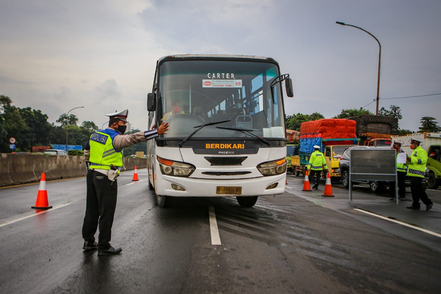 Petugas kepolisian mengarahkan bus ke pintu keluar Tol Bitung, Kabupaten Tangerang, Banten, Jumat (24/4/2020). Penyekatan itu dilakukan menyusul adanya larangan mudik bagi seluruh kalangan yang sudah ditetapkan mulai hari ini guna mencegah penyebaran COVID-19. Foto: ANTARA FOTO/Fauzan