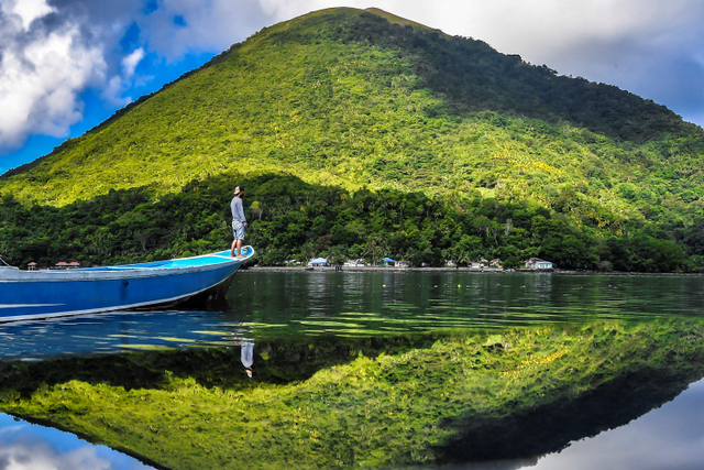 Nelayan berada di atas kapalnya dengan latar belakang Gunung Api Banda, Maluku. Foto: Muhammad Adimaja/ANTARA FOTO