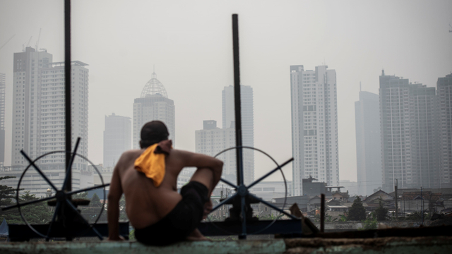 Seorang warga berjemur dengan latar belakang gedung bertingkat tersamar kabut polusi udara di Jakarta, Selasa (20/4/2021). Foto: Aprillio Akbar/ANTARA FOTO