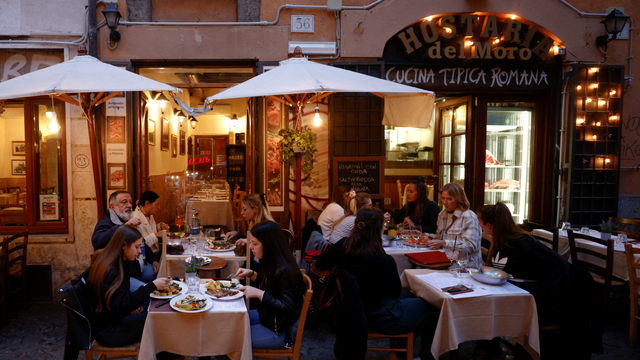 Orang-orang menikmati makanan di restoran di meja luar ruangan, di Roma, Italia, Senin (26/4). Foto: Guglielmo Mangiapane/REUTERS