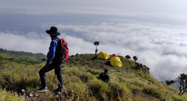 Seorang pendaki gunung dengan latar belakang area camp pos 4 dan lautan awan, jalur pendakian Sumbing via Dukuh Seman. Foto: Harley Sastha