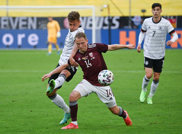 Joshua Kimmich dari Jerman dan Andrejs Ciganiks dari Latvia beraksi pada Pertandingan Persahabatan Internasional di Merkur Spiel-Arena (7/6). Foto: Federico Gambarini/Pool via REUTERS