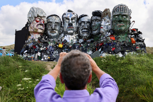 Seorang warga memotret karya seni bertajuk 'Gunung Daur Ulang' yang menggambarkan wajah para pemimpin G7 terbuat dari sampah elektronik dibuat oleh Joe Rush dan Alex Wreckage di Teluk Carbis, Hayle Towans, Cornwall, Inggris. Foto: Tom Nicholson/REUTERS