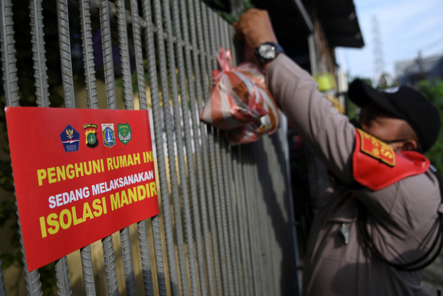 Polisi menggantungkan makanan pada pagar warga yang menjalani isolasi mandiri di kawasan Warakas, Tanjung Priok, Jakarta Utara, Selasa (22/6/2021). Foto: M Risyal Hidayat/Antara Foto