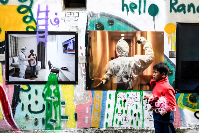 Seorang anak melintas di depan karya foto saat pameran fotografi bertajuk Meredah COVID-19 di kawasan Pasar Lama, Tangerang, Banten, Minggu (30/5). Foto: Muhammad Adimaja/ANTARA FOTO