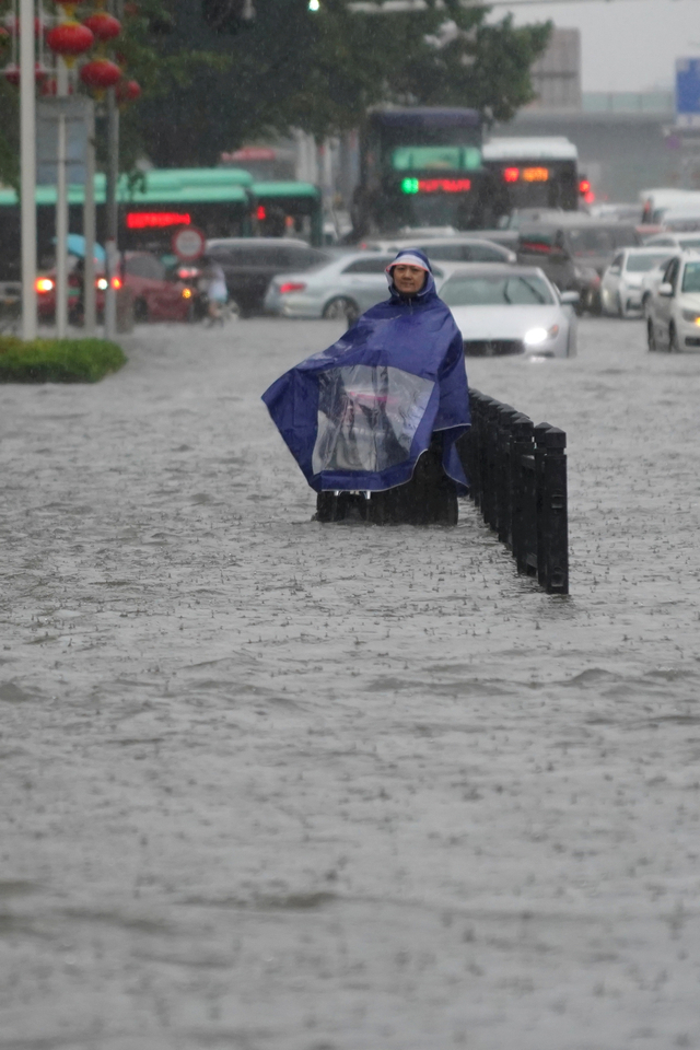 Warga mengenakan jas hujan saat mengarungi banjir di jalan di Zhengzhou, provinsi Henan, Cina, Selasa (20/7). Foto: cnsphoto via REUTERS